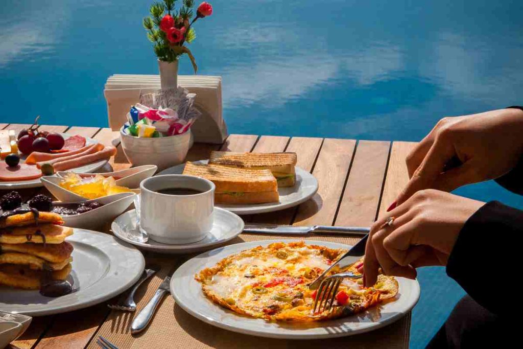 woman-eats-omelet-with-vegetables-pancakes-food-with-chocolate-cake-wooden-table
