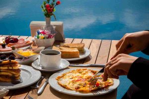 woman-eats-omelet-with-vegetables-pancakes-food-with-chocolate-cake-wooden-table