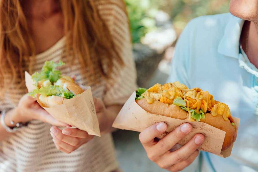 young-woman-man-holding-hot-dog-hands-eating-street-food